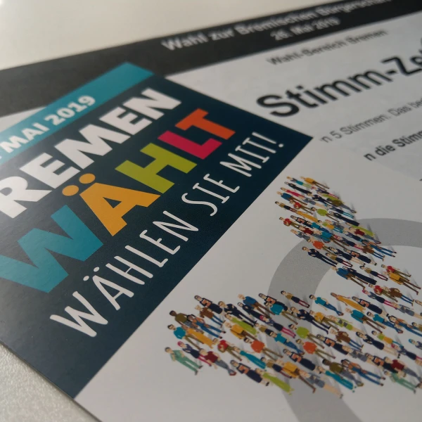 Das Bild zeigt einen Flyer für die Wahlen in Bremen am 26. Mai 2019. Auf dem Blatt steht der Slogan "BREMEN WÄHLT. Wählen Sie mit!", neben weiteren Textelementen über die Wahl. Grafisch hervorgehoben ist eine Abbildung von vielen kleinen, stilisierten Menschen, die sich an einer Wahlurne anstellen.  