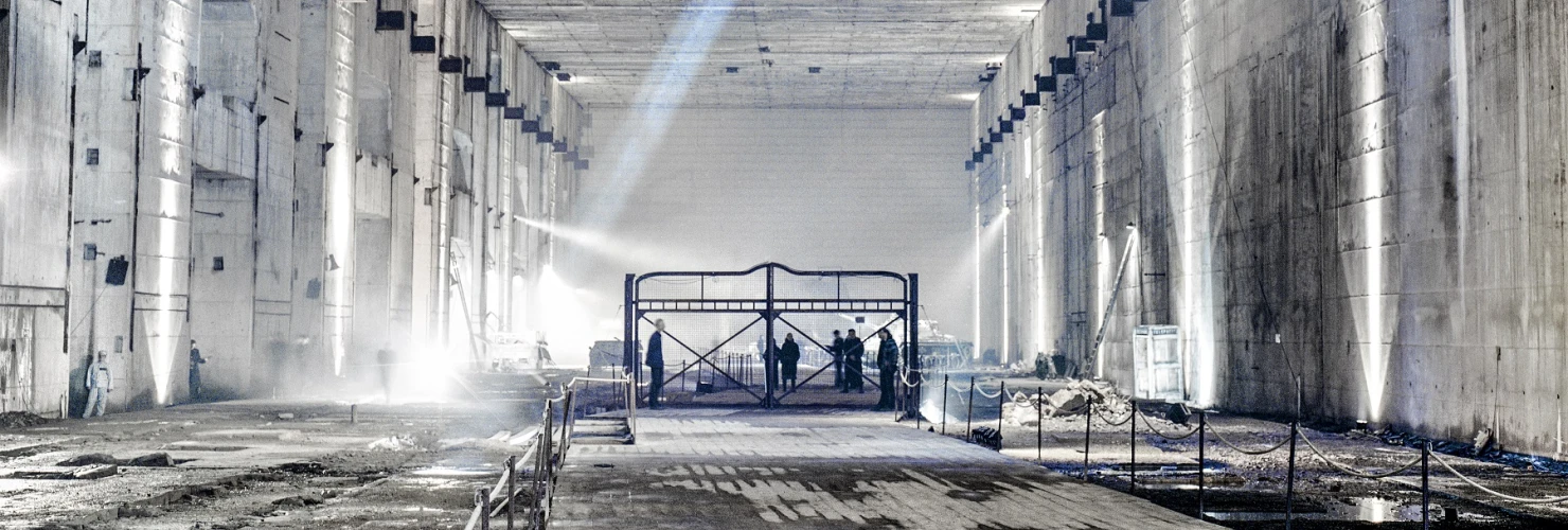 Der Ruinenteil des Bunker Valentin von innen. Im Ruinenteil stehen Menschen auf einem Gestell und ein blauer Lichtstrahl aus einem Durchschlagskrater zieht durch das Bild. Die Menschen führen die Aufführung "Die letzten Tage der Menschheit" (2001) auf  