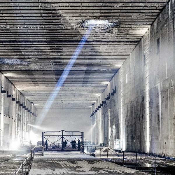 Der Ruinenteil des Bunker Valentin von innen. Im Ruinenteil stehen Menschen auf einem Gestell und ein blauer Lichtstrahl aus einem Durchschlagskrater zieht durch das Bild. Die Menschen führen die Aufführung "Die letzten Tage der Menschheit" (2001) auf  