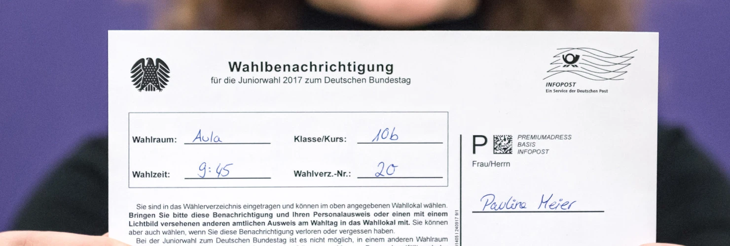 Eine Frau hält einen ausgefüllten Wahlberechtigungsschein für die Jugendwahl 2017 in die Kamera  