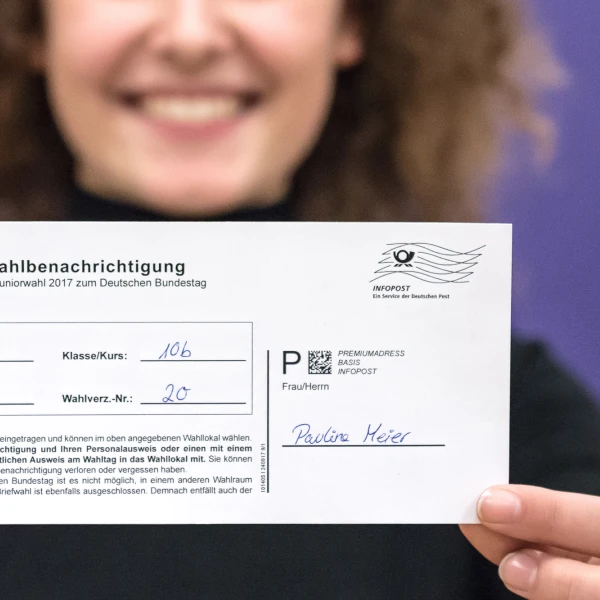Eine Frau hält einen ausgefüllten Wahlberechtigungsschein für die Juniorwahl 2017 in die Kamera  