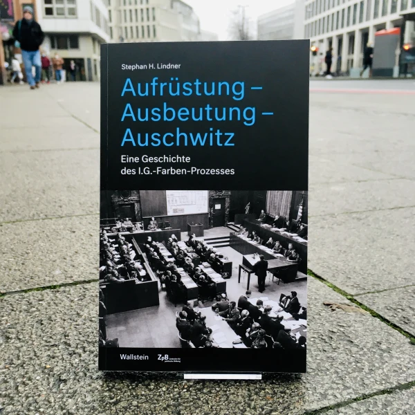 Ein Bild des Buches: "Aufrüstung-Ausbeutung-Auschwitz. Eine Geschichte des I.G. -Farben-Prozesses" von Stephan H. Lindner mit dem Hintergrund einer städtischen Straße.  