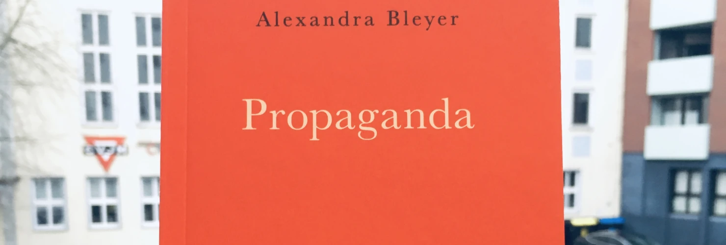 Ein Bild des Buches: "Propaganda" von Alexandra Bleyer mit dem Hintergrund von Gebäuden.  