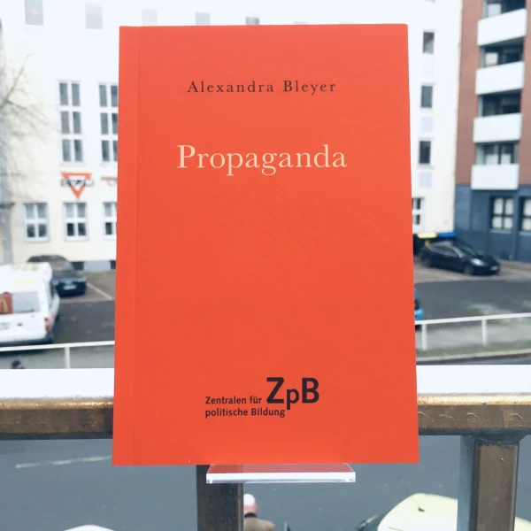 Ein Bild des Buches: "Propaganda" von Alexandra Bleyer mit dem Hintergrund von Gebäuden.  