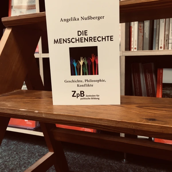 Ein Bild des Buches "Die Menschenrechte. Geschichte, Philosophie, Konflikte" von Angelika Nußberger mit dem Hintergrund aus Bücherregalen.    