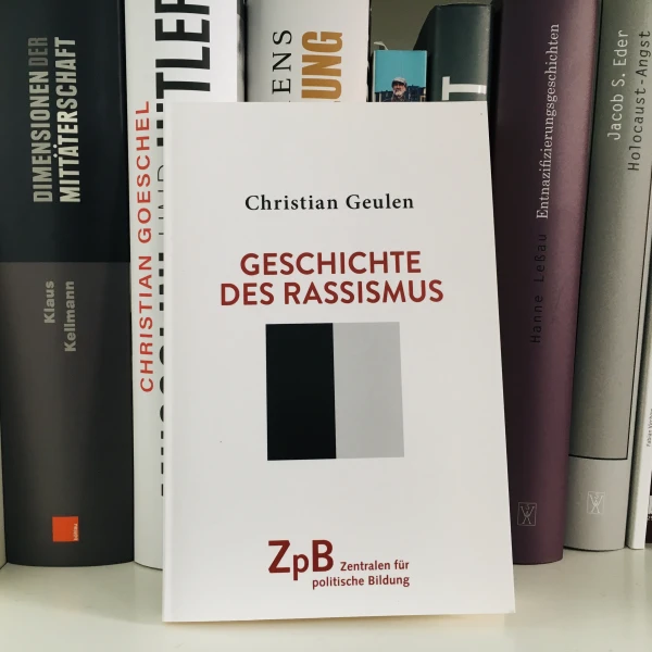 Ein Bild des Buches "Geschichte des Rassismus" von Christian Geulen mit einem Hintergrund aus Büchern.   