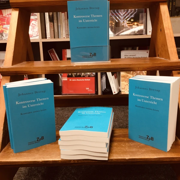 Ein Bild der Bücher: " Kontroverse Themen im Unterricht. Konstruktiv streiten lernen" von Johannes Drerup mit einem Hintergrund aus Bücherregalen.   