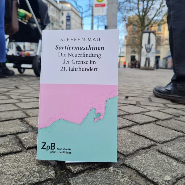 Ein Bild des Buches "Sortiermaschinen-Die Neuerfindung der Grenze im 21. Jahrhundert" von Steffen Mau mit einem Hintergrund einer städtischen Straße.  