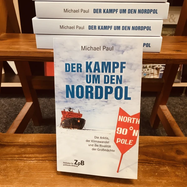 Ein Bild des Buches: " Der Kampf um den Nordpol- Die Arktis, Der Klimawandel und die Rivalität der Großmächte" von Michael Paul mit dem Hintergrund eines Bücherregals.  