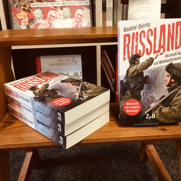 Das Cover des Buches "Russland - Ukrainekrieg und Weltmachtträume" mit einer Fotoillustration von Soldaten in Militärkleidung und mit Maschinengewehren. Ein Soldat im Hintergrund malt mit roter Farbe ein Wandbild an die Wand. Das Wandbild zei  