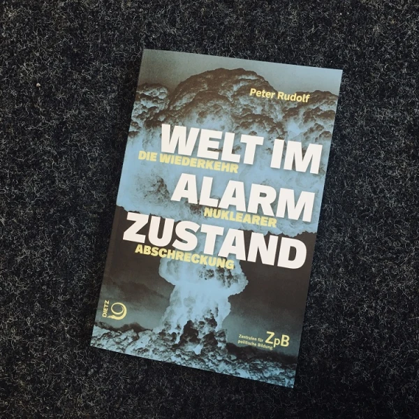 Ein Bild des Buchcovers: " Welt im Alarmzustand. Die Wiederkehr nuklearer Abschreckung" mit dem Foto einer Atombombenexplosion. Der Titel auf dem Buch ist weiß und gelb geschrieben.  