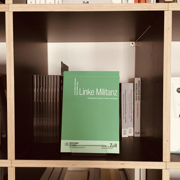 Ein Bild des Buches: "Linke Militanz"-Pädagogische Arbeit in Theorie und Praxis, mit dem Hintergrund von Büchern.