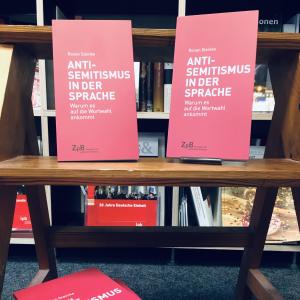 Ein Bild der Bücher: "Antisemitismus in der Sprache" von Ronen Steinke mit dem Hintergrund aus Bücherregalen. 