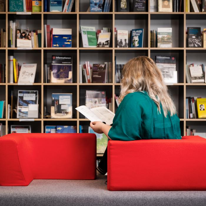 Eine Frau, die auf einer roten Couch sitzt und ein Buch in der Bibliothek liest.