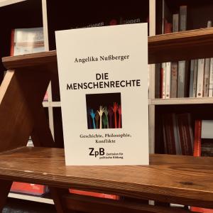 Ein Bild des Buches "Die Menschenrechte. Geschichte, Philosophie, Konflikte" von Angelika Nußberger mit dem Hintergrund aus Bücherregalen.  