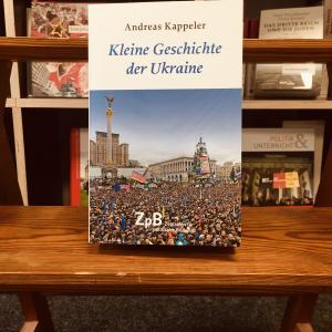 Zu sehen ist ein Buchcover "Kleine Geschichte der Ukraine" mit einem Foto einer Demonstration von Tausenden von Menschen, die auf dem Hauptplatz von Kiew, dem "Maidan", stehen und verschiedene Fahnen schwenken. 