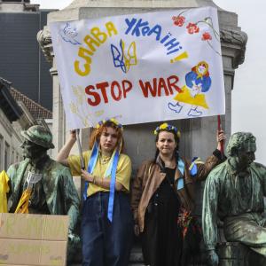 Eine Gruppe von Menschen steht vor einer Statue und hält ein Plakat mit einem Text: "Slava Ukraini, stop war"